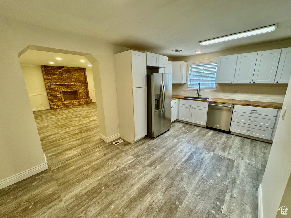 Kitchen featuring butcher block counters, appliances with stainless steel finishes, light hardwood / wood-style flooring, a fireplace, and sink