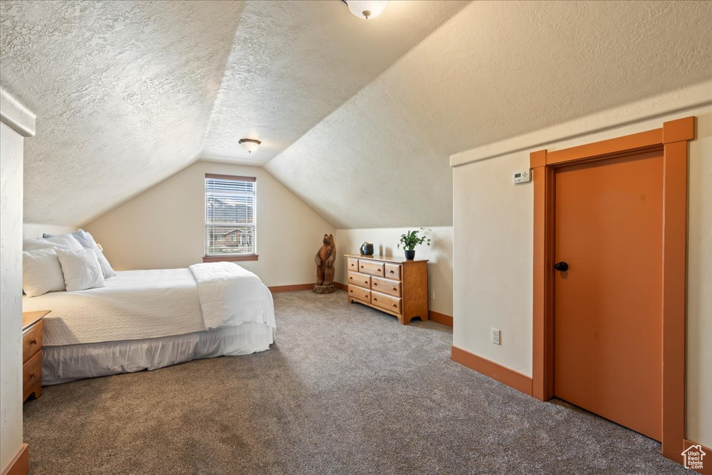 Bedroom with a textured ceiling, vaulted ceiling, and carpet