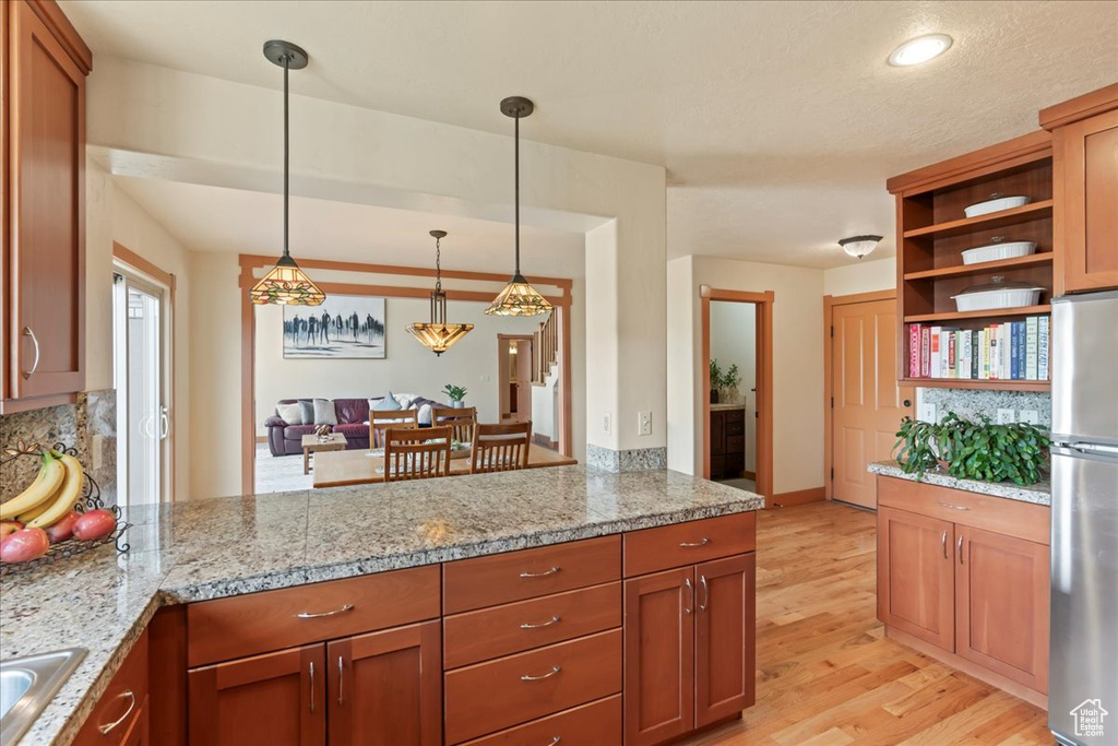 Kitchen featuring hanging light fixtures, light hardwood / wood-style flooring, light stone countertops, and stainless steel refrigerator