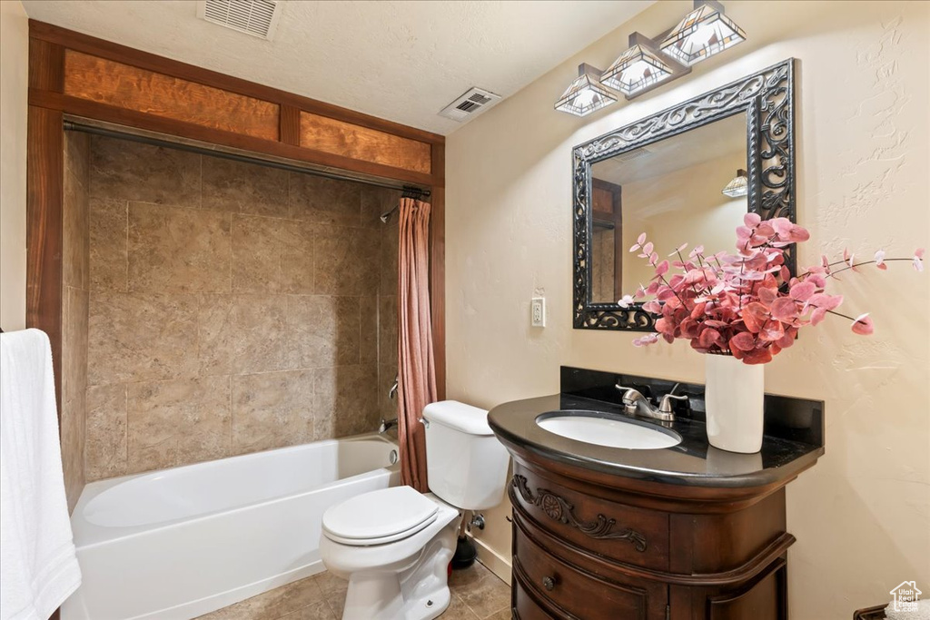 Full bathroom with tile floors, vanity, shower / bathtub combination with curtain, toilet, and a textured ceiling