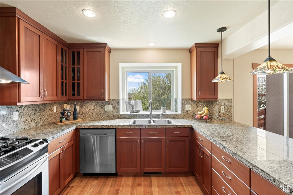 Kitchen with decorative light fixtures, light hardwood / wood-style floors, dishwasher, and backsplash