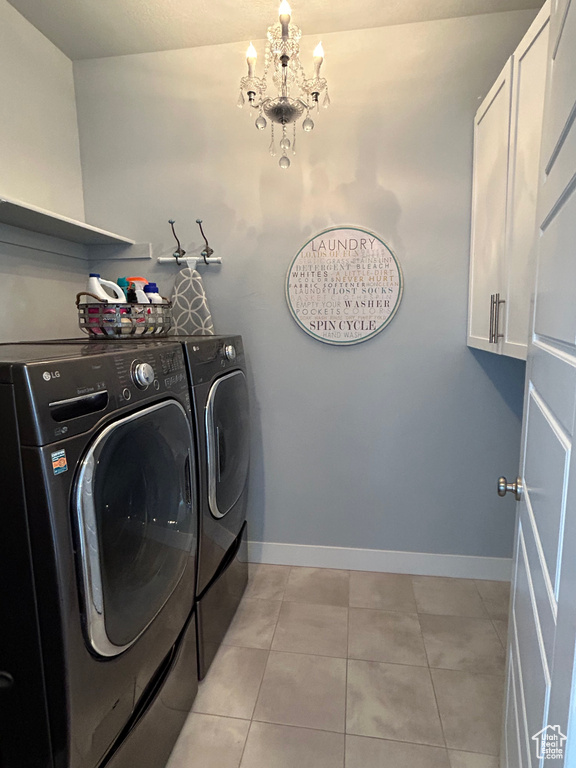 Clothes washing area featuring a chandelier, washer and dryer, cabinets, and light tile flooring