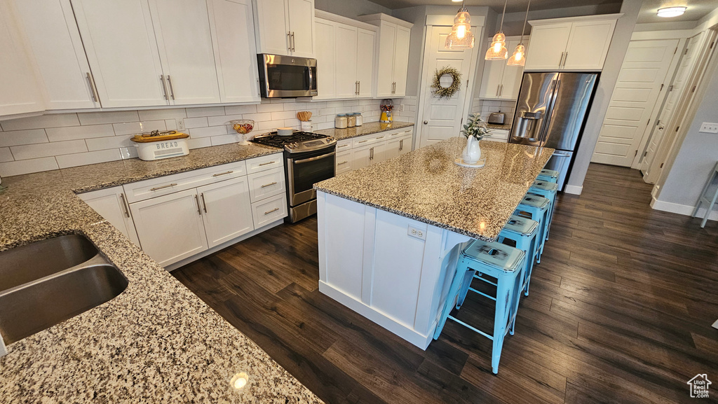 Kitchen featuring appliances with stainless steel finishes, a kitchen island, a kitchen bar, tasteful backsplash, and dark hardwood / wood-style flooring