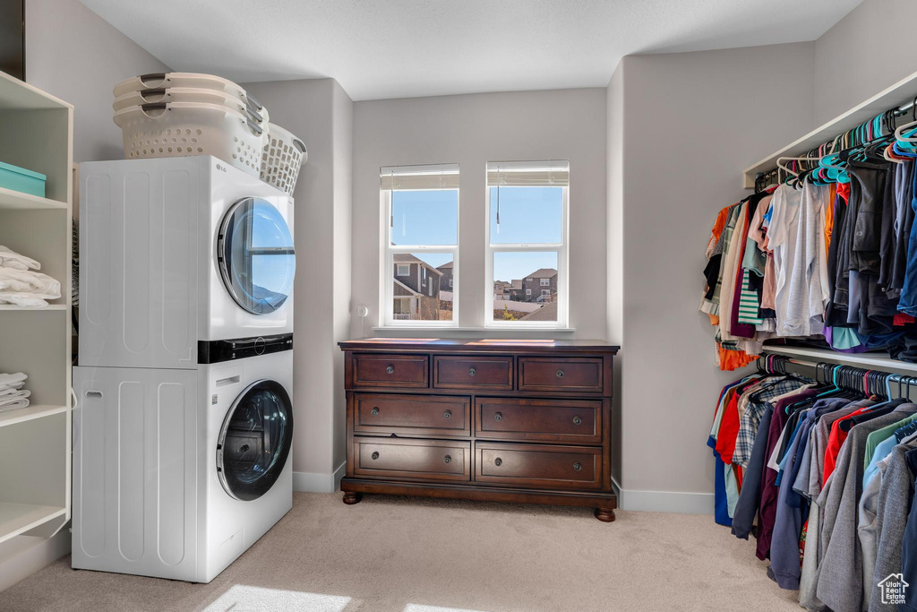 Clothes washing area with light colored carpet and stacked washer and dryer