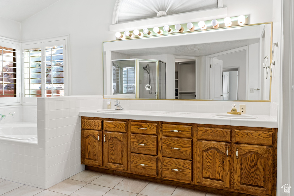 Bathroom with vaulted ceiling, vanity with extensive cabinet space, tile flooring, double sink, and plus walk in shower