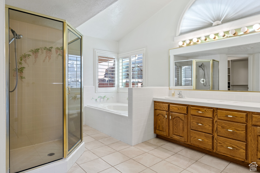 Bathroom with lofted ceiling, separate shower and tub, vanity with extensive cabinet space, and tile flooring