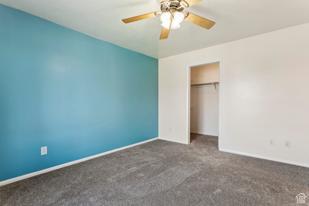 Unfurnished bedroom with a closet, dark carpet, and ceiling fan