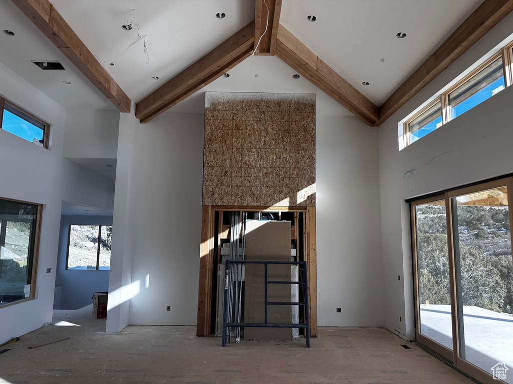 Unfurnished living room featuring beamed ceiling and a towering ceiling