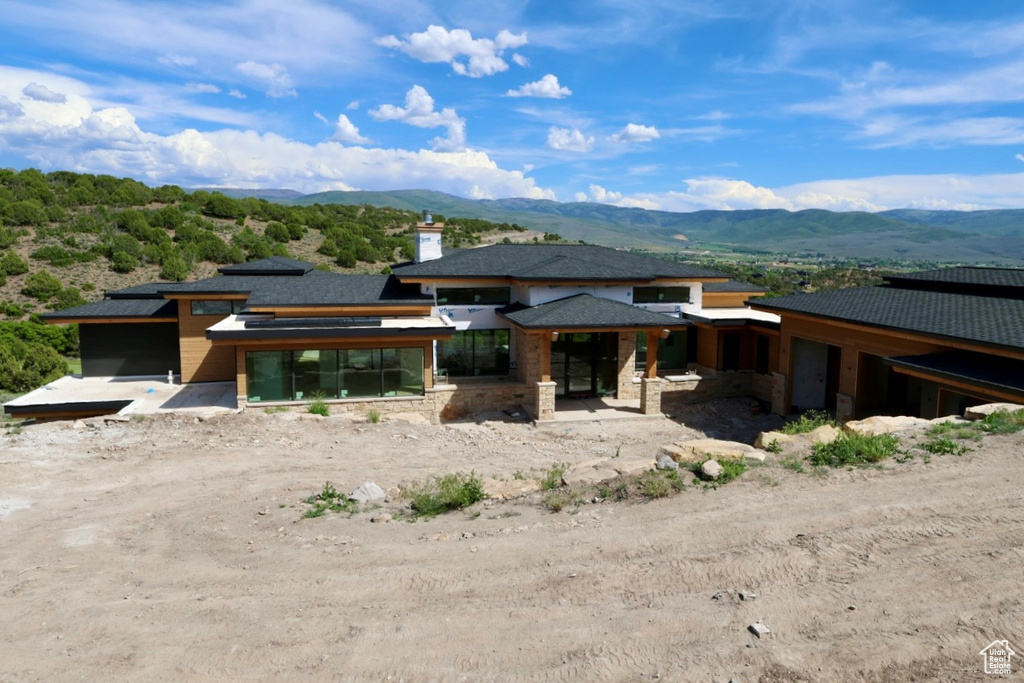 Back of house with a mountain view, a sunroom, stone siding, and a chimney