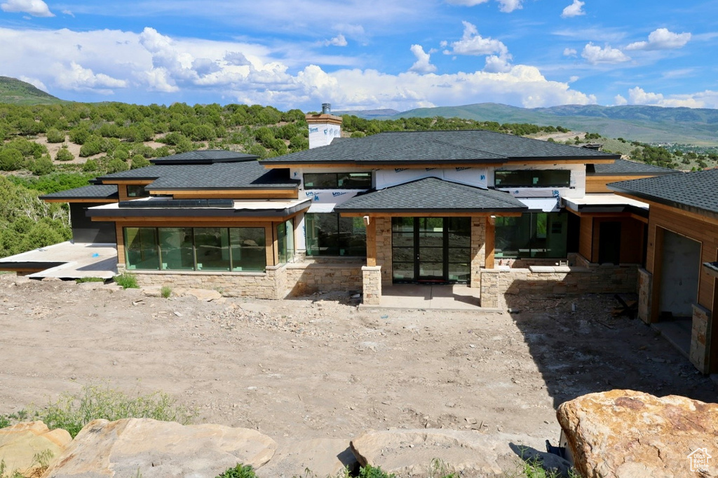 Rear view of property with a mountain view, stone siding, and a patio area