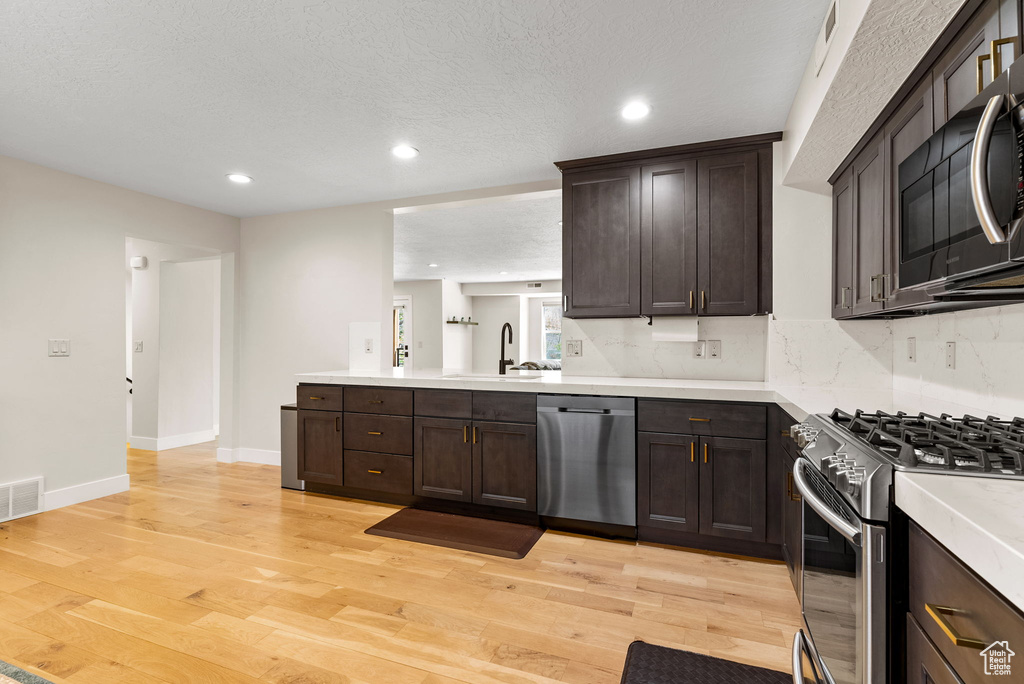 Kitchen featuring dark brown cabinets, appliances with stainless steel finishes, backsplash, sink, and light wood-type flooring