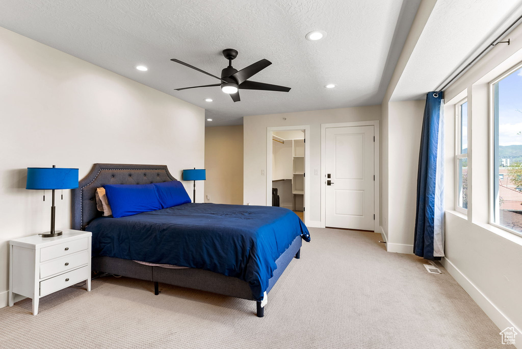 Bedroom with a closet, a spacious closet, light colored carpet, ceiling fan, and a textured ceiling
