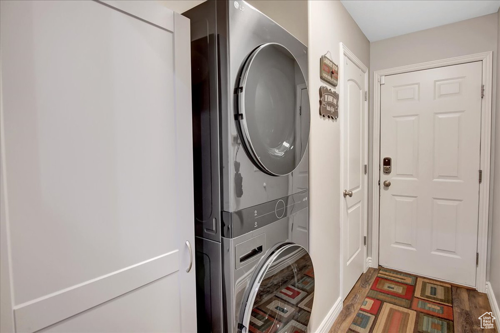 Clothes washing area with dark hardwood / wood-style floors and stacked washer and dryer