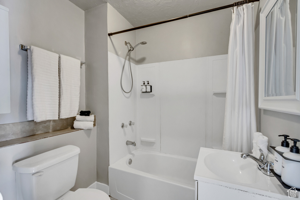 Full bathroom with a textured ceiling, vanity, shower / bathtub combination with curtain, and toilet