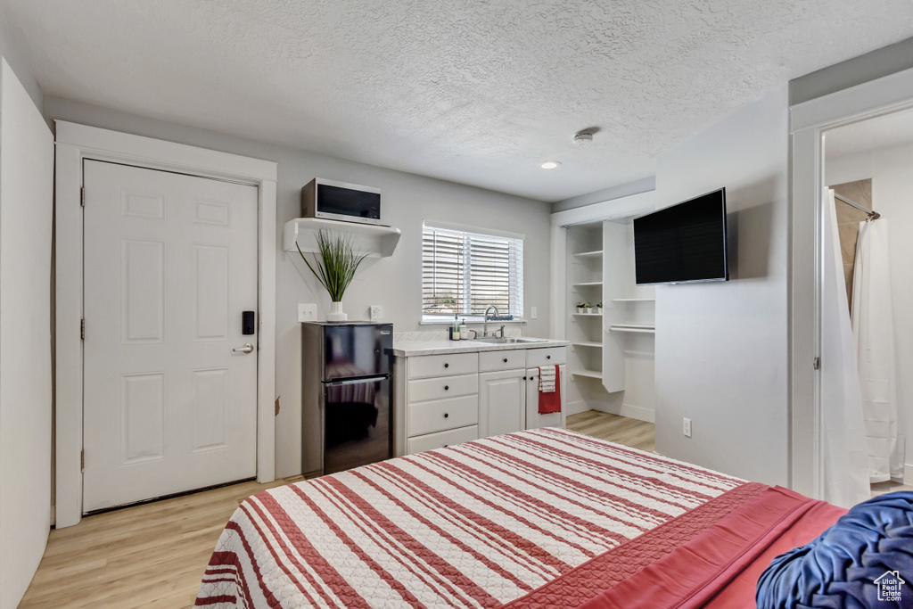 Bedroom with a textured ceiling, sink, light hardwood / wood-style floors, and black fridge