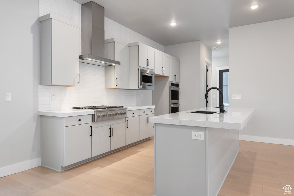 Kitchen featuring backsplash, wall chimney range hood, stainless steel appliances, sink, and light hardwood / wood-style floors