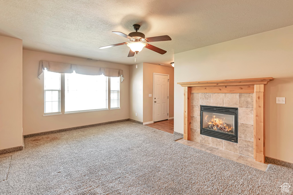 Unfurnished living room featuring light colored carpet, a textured ceiling, ceiling fan, and a tiled fireplace