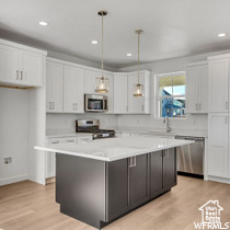 Kitchen with stainless steel appliances, a center island, light wood-type flooring, and white cabinetry