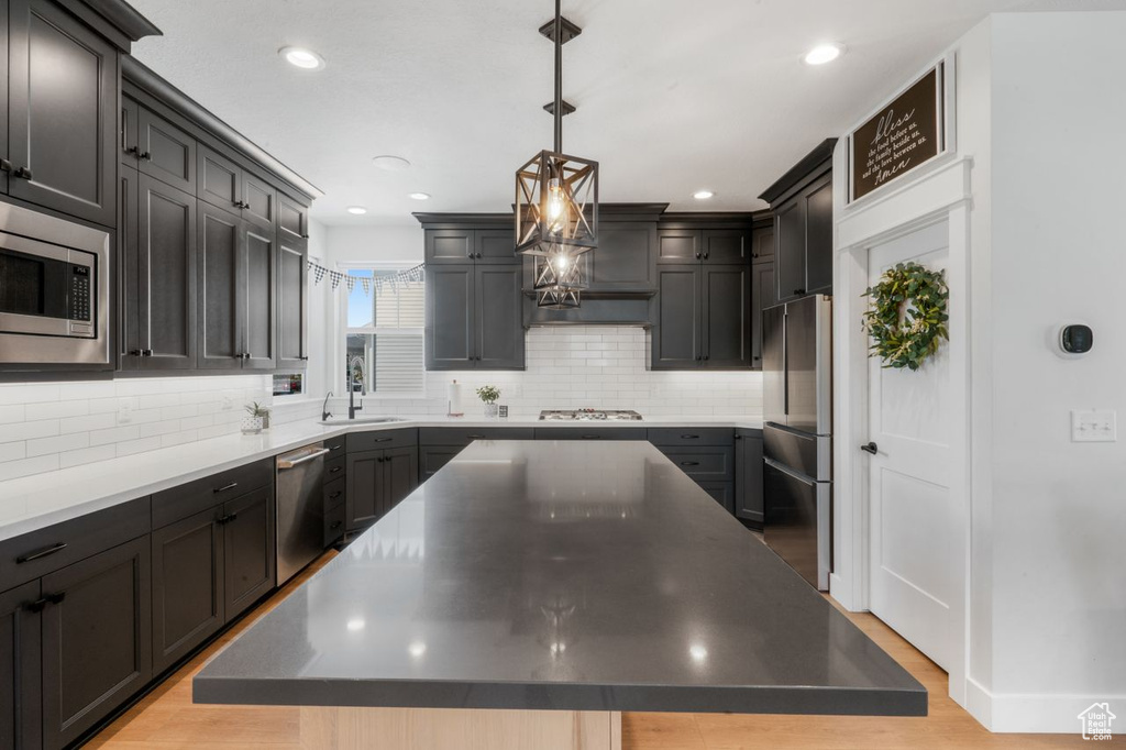 Kitchen featuring a center island, tasteful backsplash, light wood-type flooring, stainless steel appliances, and pendant lighting