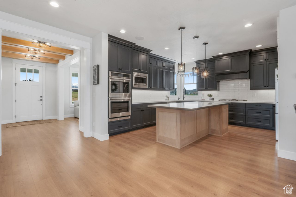 Kitchen featuring appliances with stainless steel finishes, a kitchen island, backsplash, light wood-type flooring, and hanging light fixtures