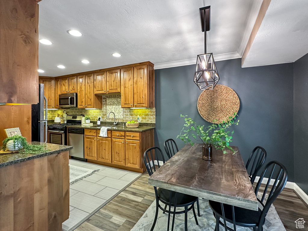 Kitchen featuring hanging light fixtures, stainless steel appliances, light tile flooring, tasteful backsplash, and dark stone counters