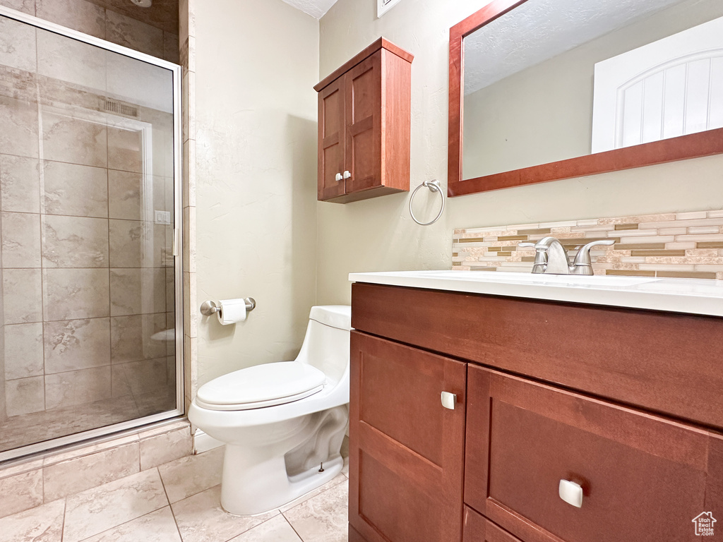 Bathroom with vanity, backsplash, a shower with shower door, tile flooring, and toilet