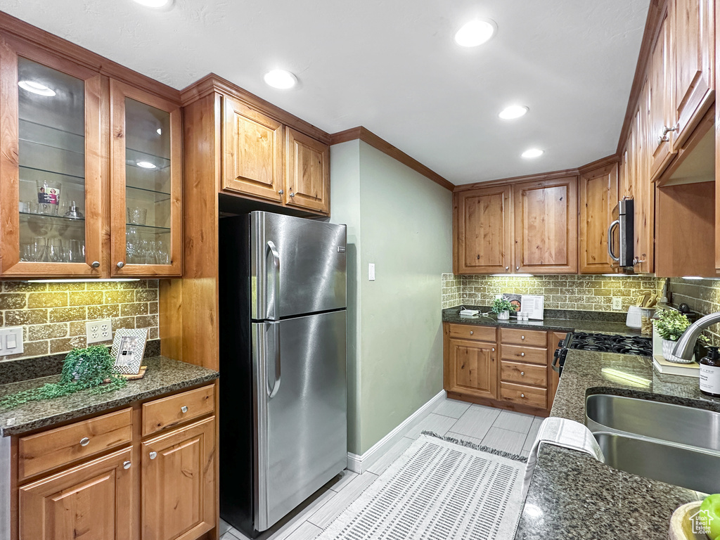 Kitchen featuring appliances with stainless steel finishes, sink, light tile flooring, tasteful backsplash, and dark stone countertops