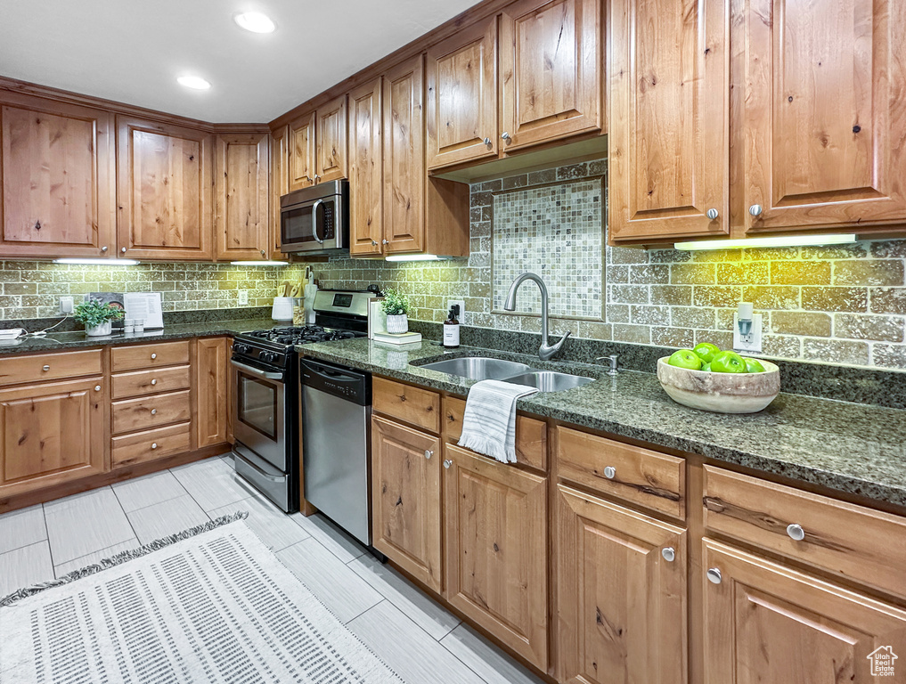 Kitchen featuring stainless steel appliances, tasteful backsplash, dark stone countertops, sink, and light tile floors