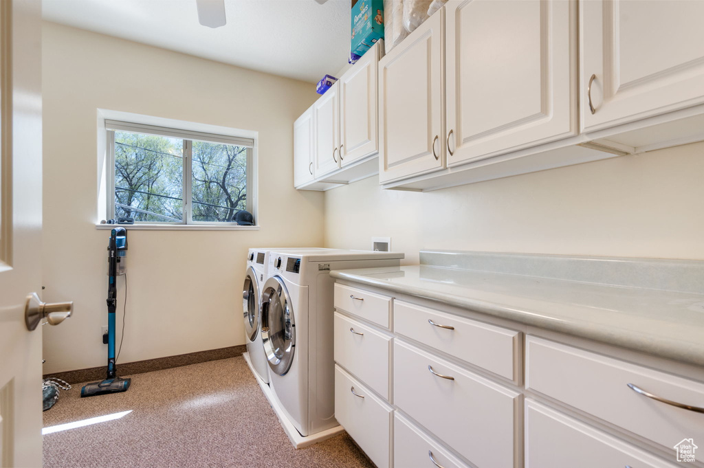 Clothes washing area with washer and clothes dryer, light carpet, and cabinets