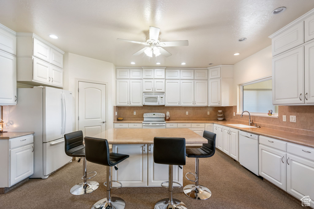 Kitchen with ceiling fan, a breakfast bar, white cabinets, sink, and white appliances