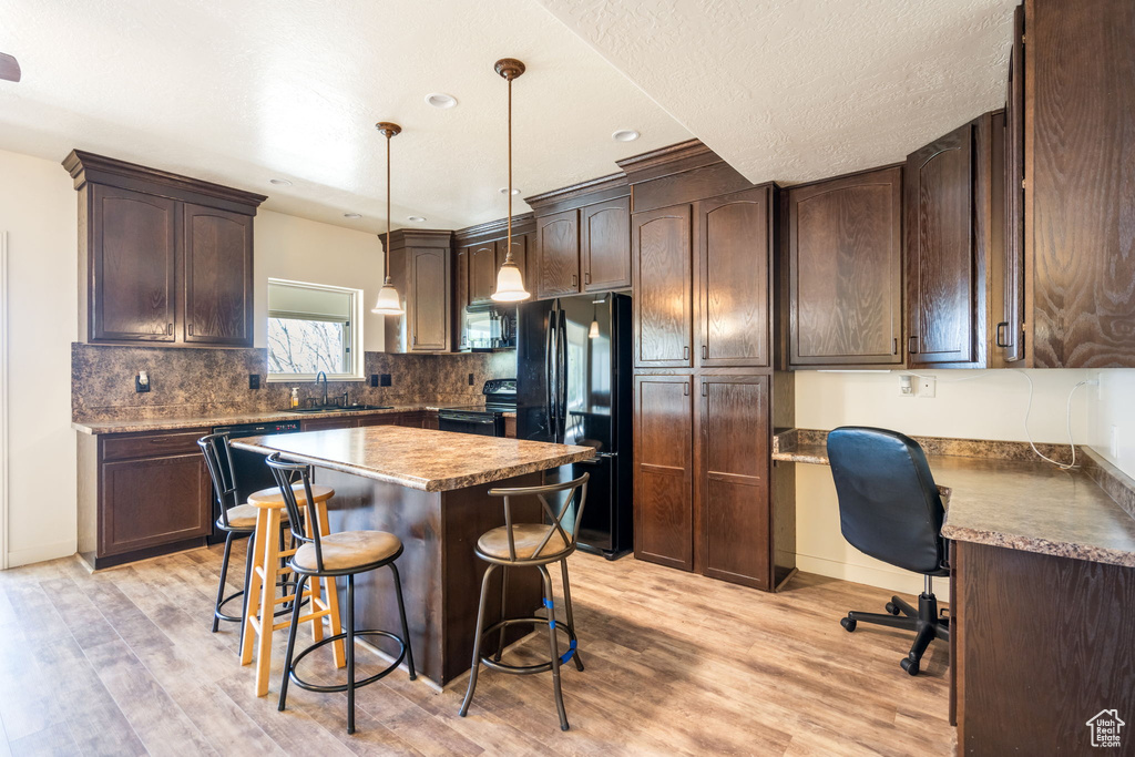 Kitchen with a kitchen island, light wood-type flooring, decorative light fixtures, black appliances, and a kitchen breakfast bar