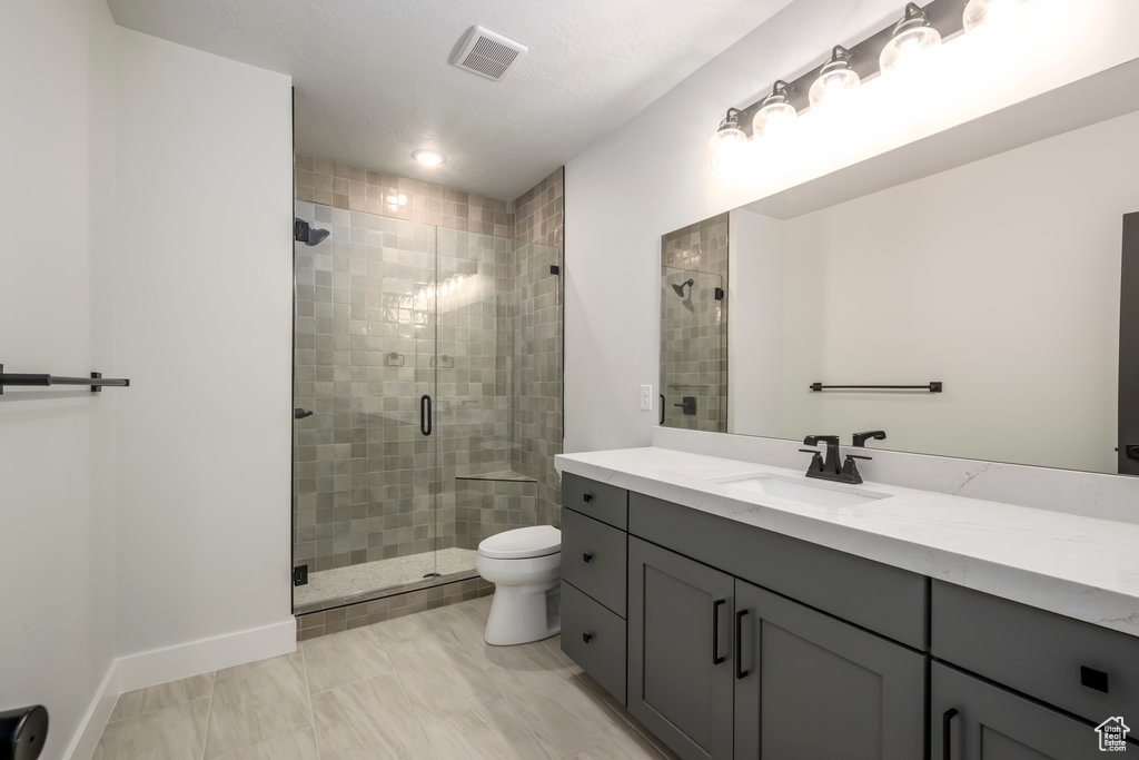 Bathroom with a shower with door, tile floors, toilet, and vanity with extensive cabinet space