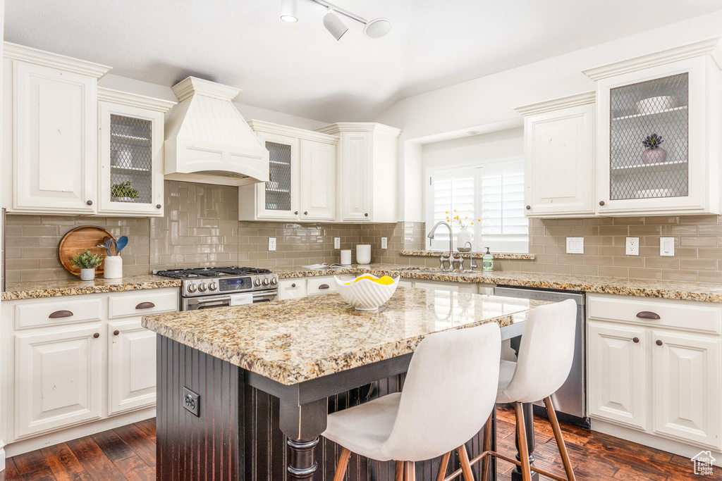 Kitchen with white cabinets, backsplash, stainless steel appliances, and custom exhaust hood
