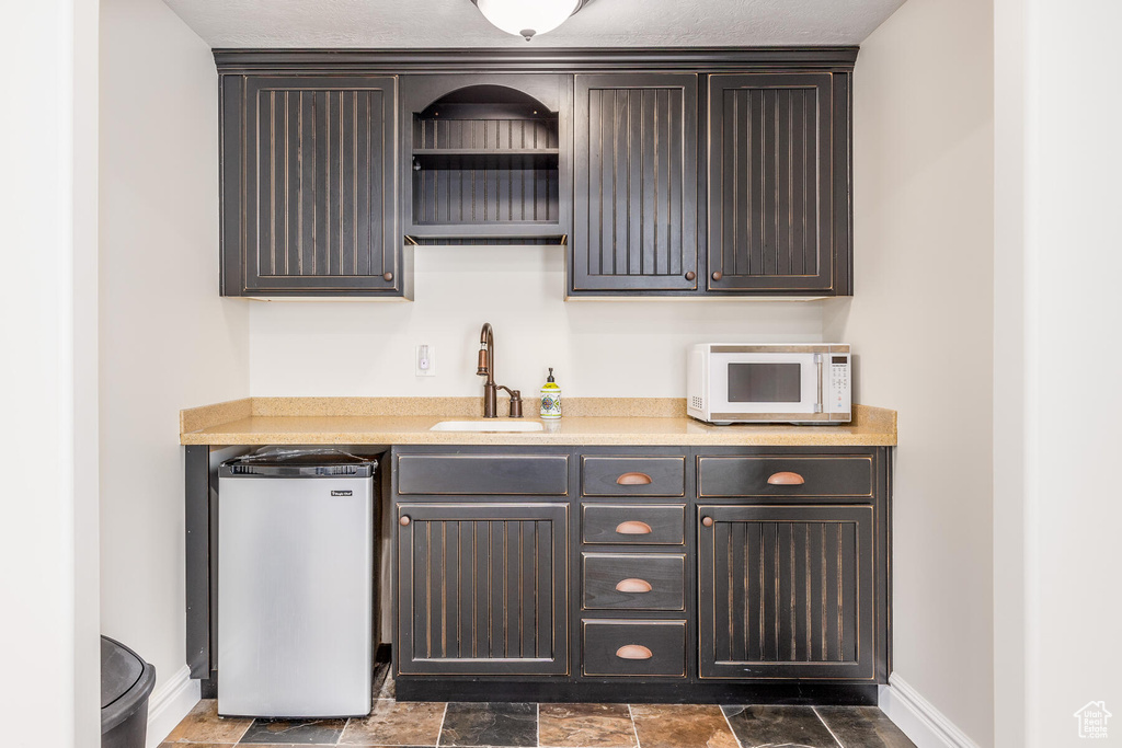Bar featuring fridge, sink, dark tile flooring, and dark brown cabinets