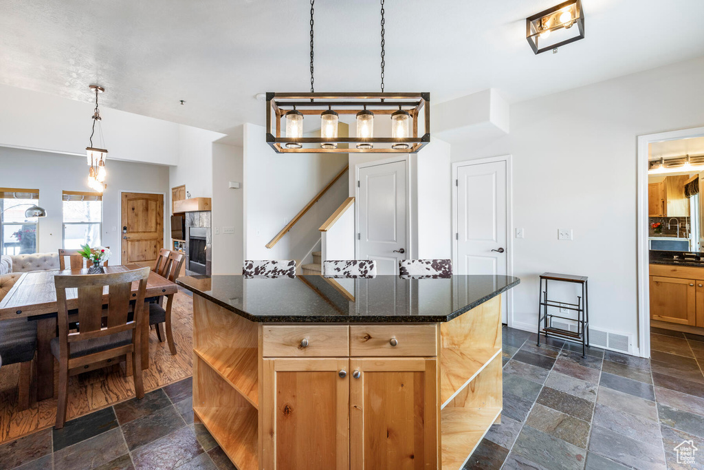 Kitchen featuring hanging light fixtures, dark tile flooring, a kitchen island, and dark stone counters