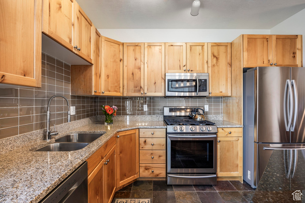 Kitchen with tasteful backsplash, stainless steel appliances, light stone countertops, and sink
