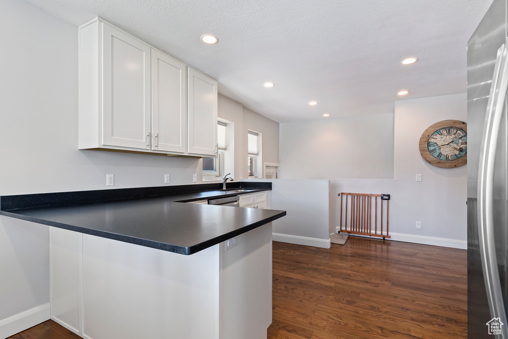 Kitchen featuring stainless steel refrigerator, dark hardwood / wood-style flooring, white cabinetry, kitchen peninsula, and sink