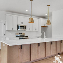 Kitchen featuring pendant lighting, stove, white cabinets, light wood-type flooring, and sink