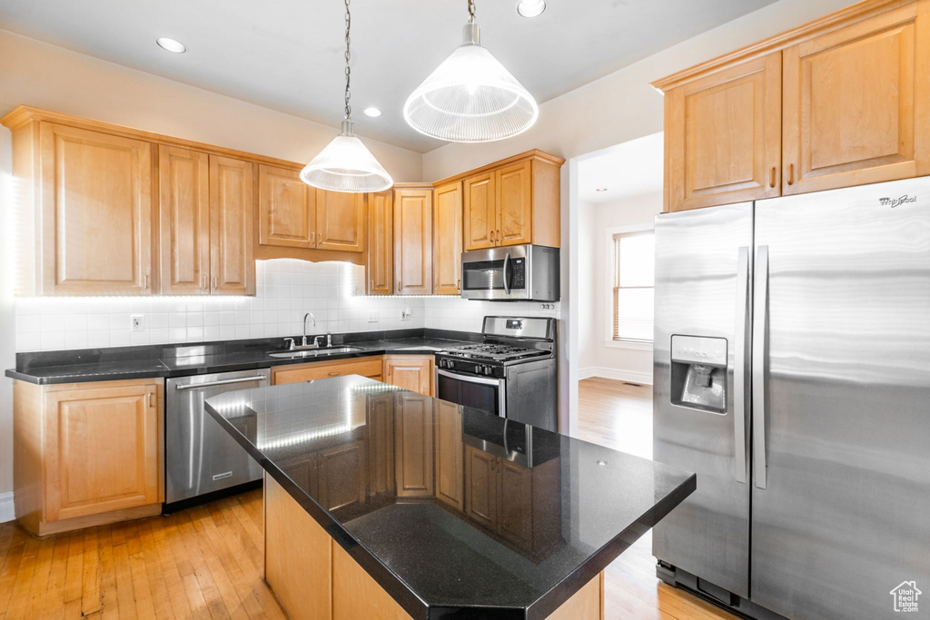 Kitchen featuring appliances with stainless steel finishes, a center island, tasteful backsplash, light wood-type flooring, and decorative light fixtures