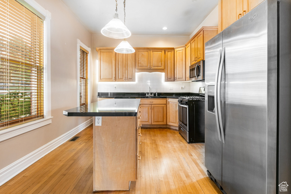 Kitchen with a kitchen island, backsplash, decorative light fixtures, stainless steel appliances, and light hardwood / wood-style flooring