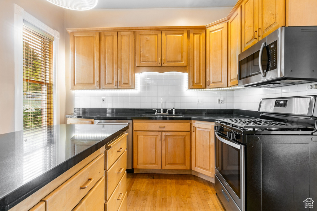 Kitchen featuring appliances with stainless steel finishes, sink, tasteful backsplash, and light wood-type flooring