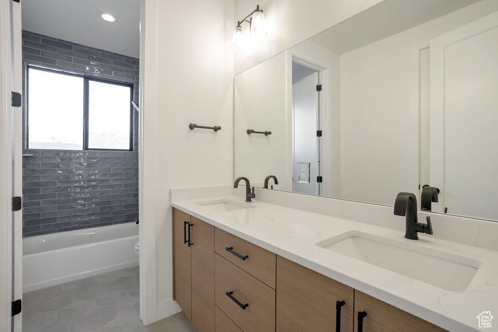 Full bathroom featuring dual bowl vanity, toilet, tile flooring, and tiled shower / bath combo