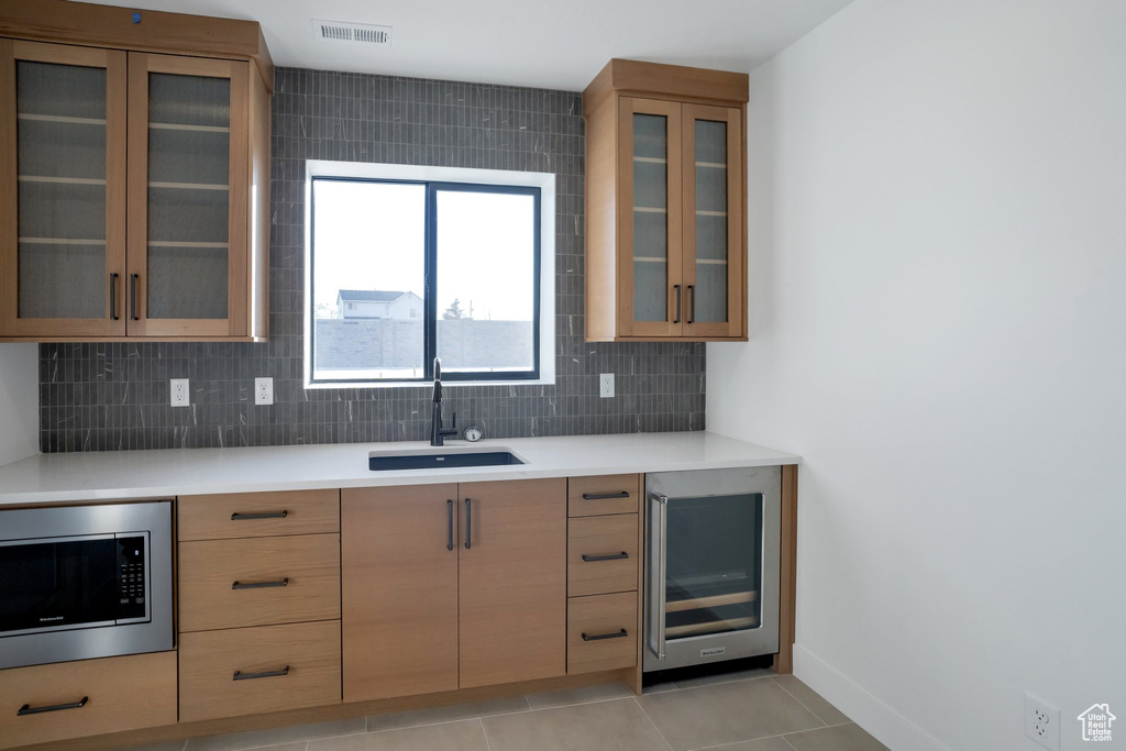 Kitchen with wine cooler, light tile flooring, stainless steel microwave, sink, and tasteful backsplash