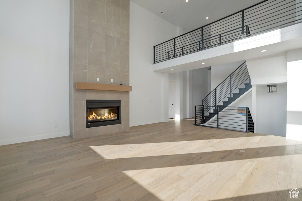 Unfurnished living room featuring light hardwood / wood-style flooring, a tile fireplace, and a high ceiling