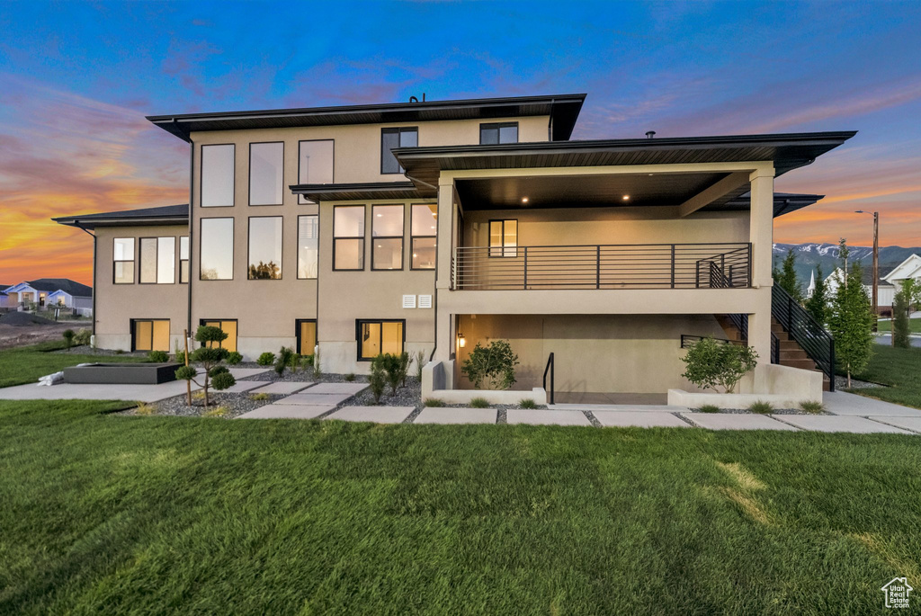 Back house at dusk with a yard and a balcony