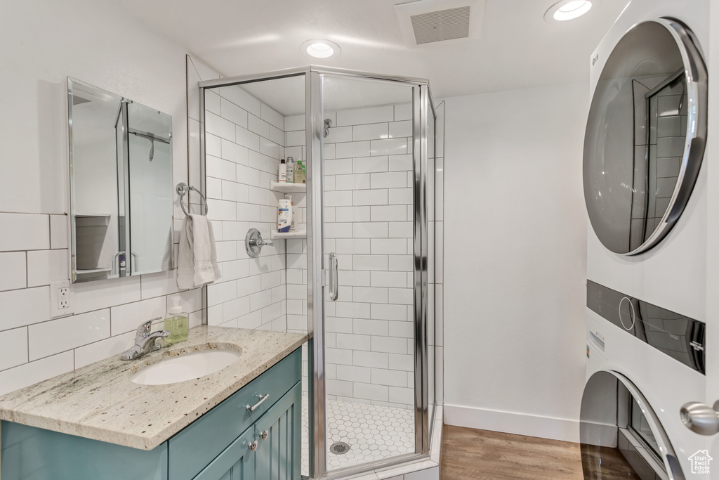 Bathroom featuring a shower with shower door, tasteful backsplash, vanity, hardwood / wood-style floors, and stacked washer and clothes dryer