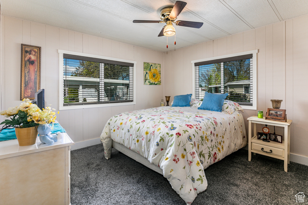 Carpeted bedroom with wooden walls, ceiling fan, and multiple windows