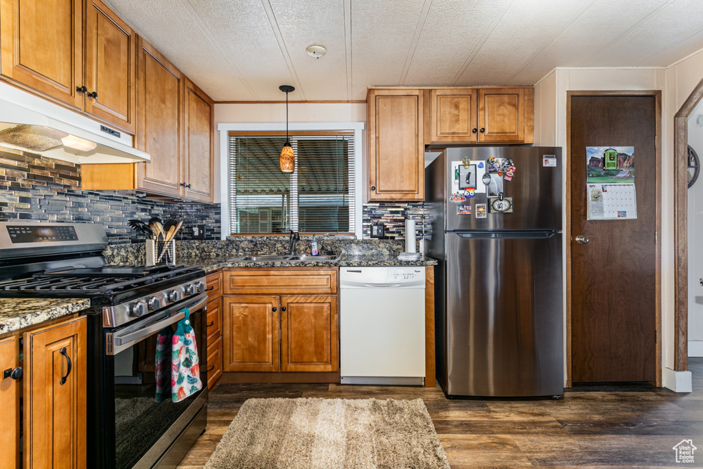 Kitchen featuring range with gas cooktop, dark wood-type flooring, stainless steel fridge, dark stone countertops, and white dishwasher