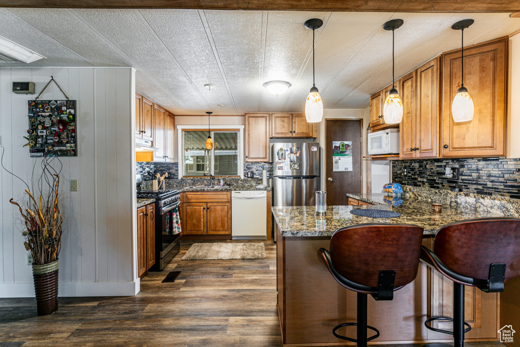 Kitchen featuring light stone counters, range hood, dark hardwood / wood-style flooring, stainless steel appliances, and pendant lighting