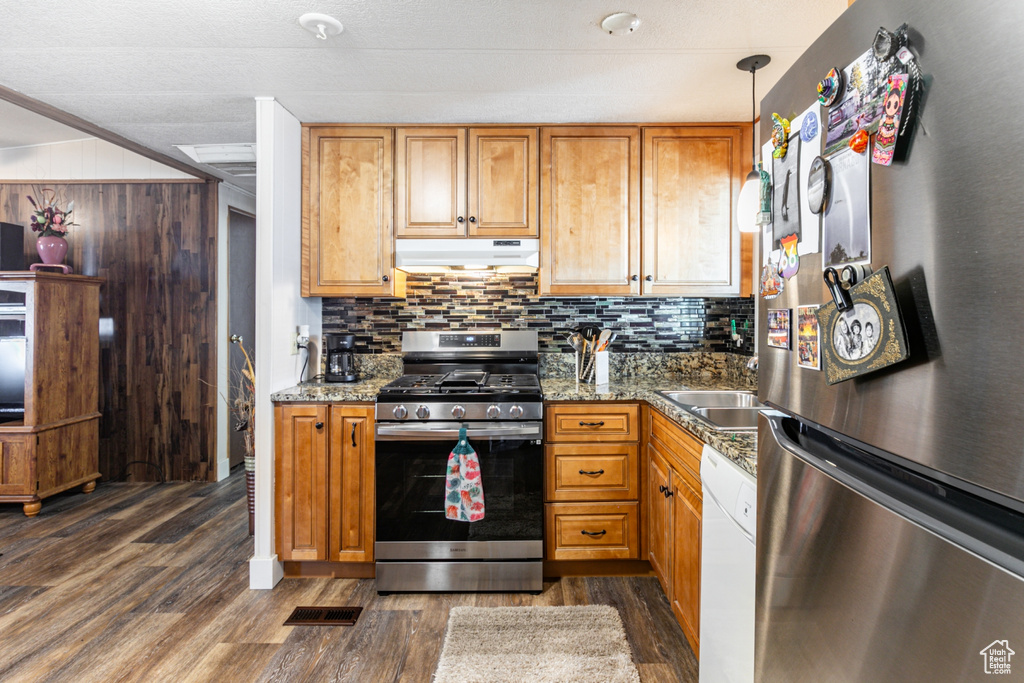 Kitchen with appliances with stainless steel finishes, backsplash, hanging light fixtures, dark hardwood / wood-style floors, and dark stone countertops